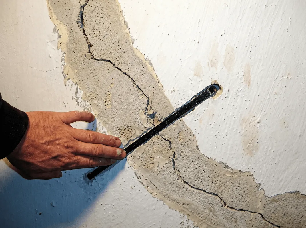 A wall with a large crack is being inspected by a professional in Jersey City, NJ